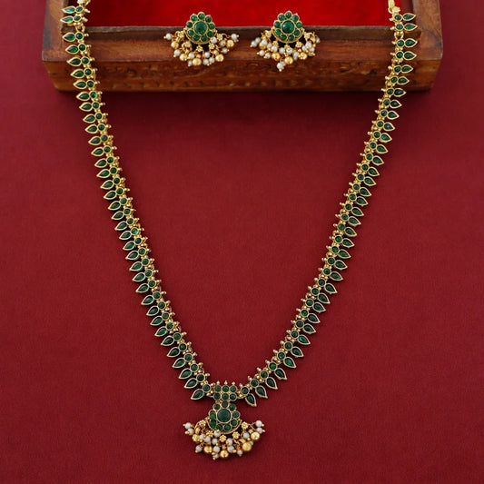 Gold and emerald green jewelry set featuring a necklace and matching earrings, displayed on a wooden stand against a deep red background.