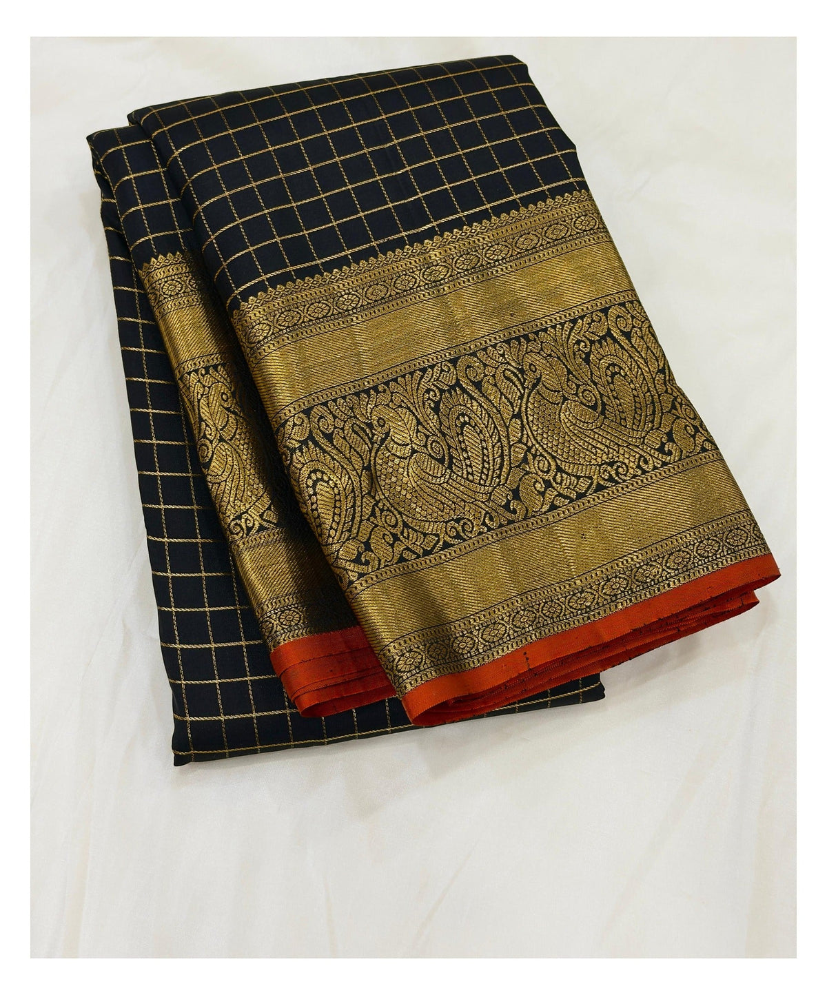 Handwoven Kanchipuram silk saree folded, showing black checked body and ornate gold-toned peacock border