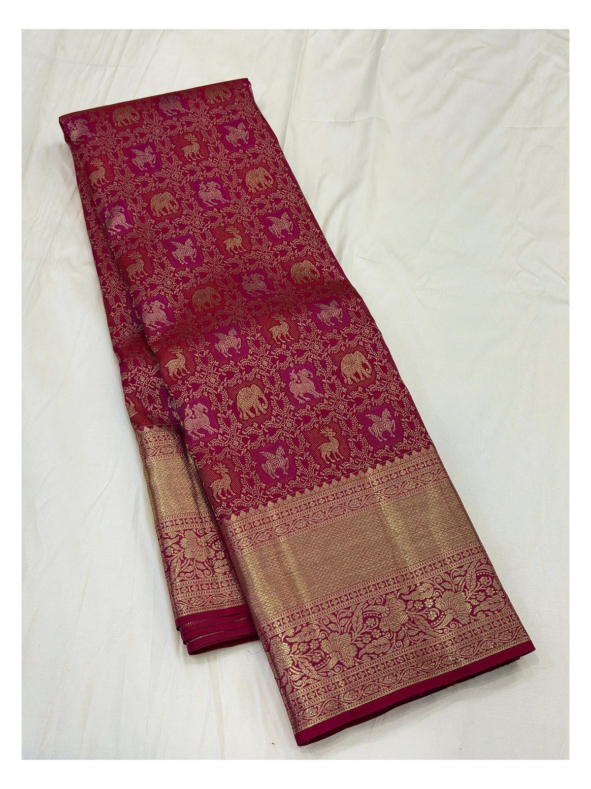 Full view of deep magenta saree with gold-toned animal motifs and wide woven border