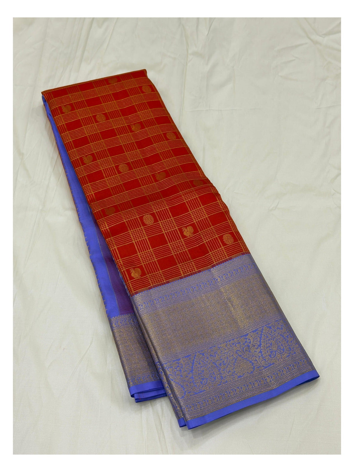 Folded handwoven Kanchipuram silk saree showing red checks and lavender zari pallu