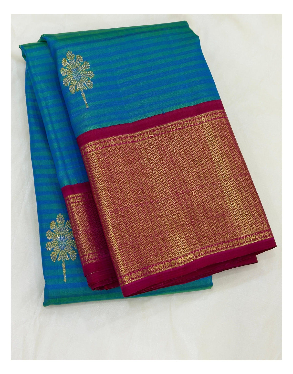 Folded teal blue Kanchipuram silk saree with magenta and gold-toned woven border