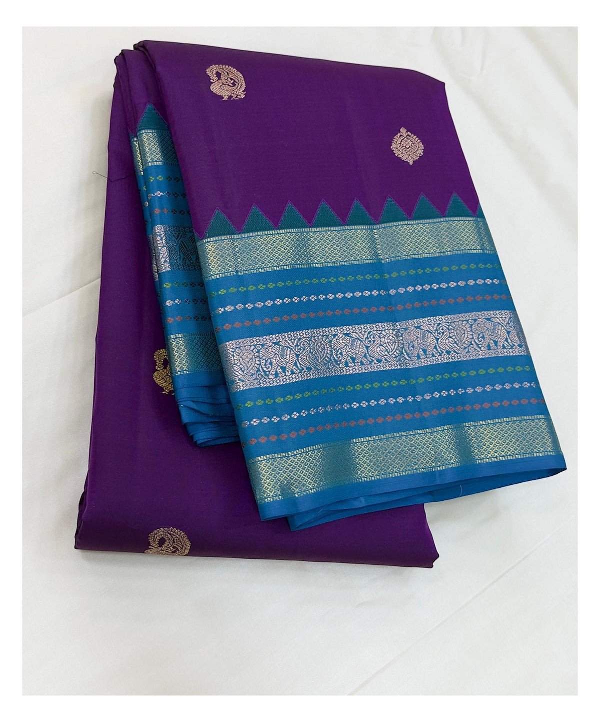Folded handwoven Kanchipuram silk saree in purple with teal blue contrast border and woven pallu