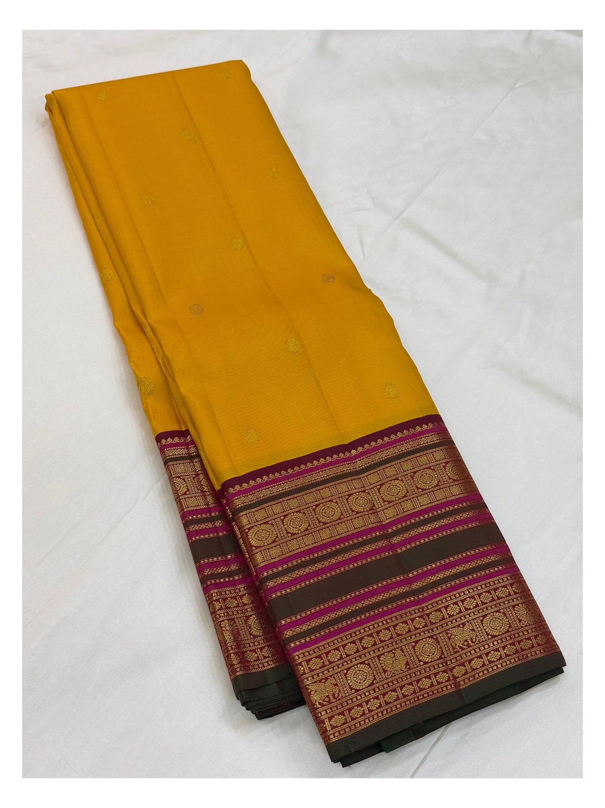 Mustard yellow handwoven Kanchipuram silk saree folded with visible woven butta motifs and contrast border
